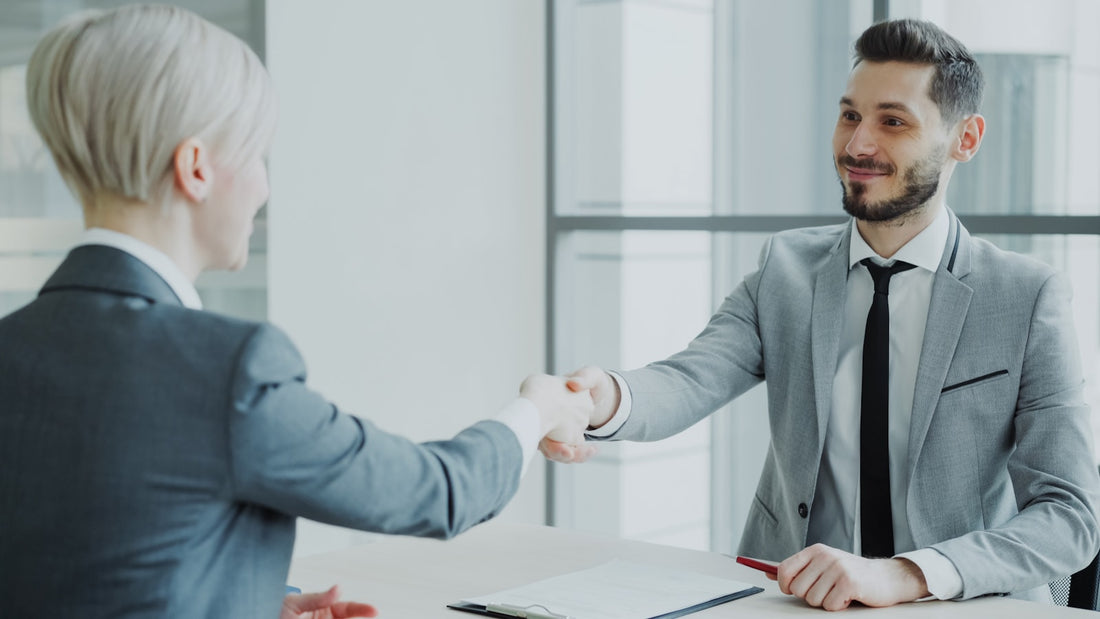 Two professionals shaking hands across a desk in a modern Dubai office, signing an employment contract